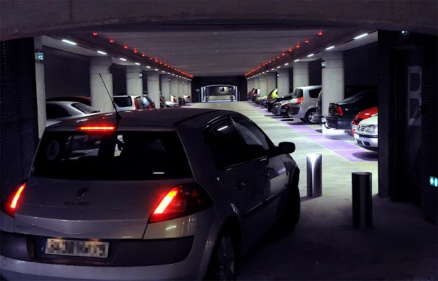 Voiture sort d'un parking souterrain, avec des lumières rouges indiquant les emplacements disponibles.