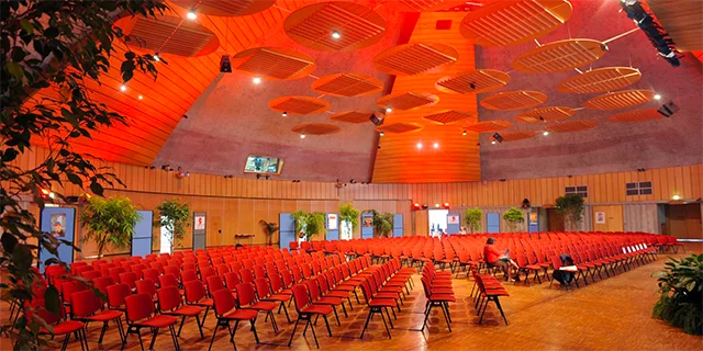 Salle de conférence avec des chaises rouges alignées et un éclairage orangé, préparée pour un événement.