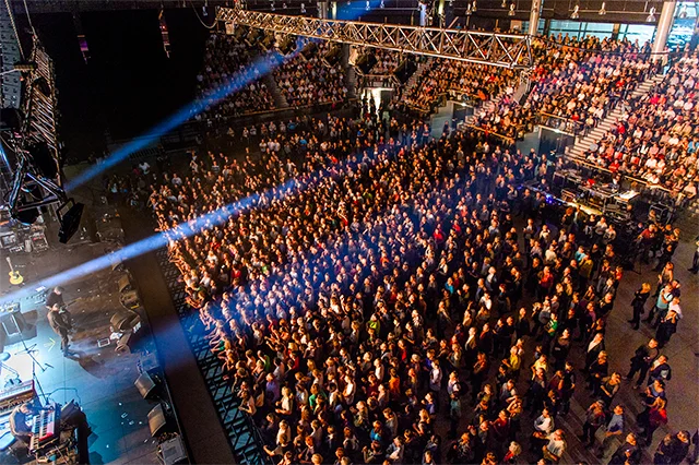 Un public nombreux assiste à un concert, captivé par la performance sur scène et les lumières.